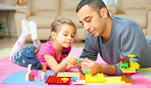 A father and daughter play with legos together.